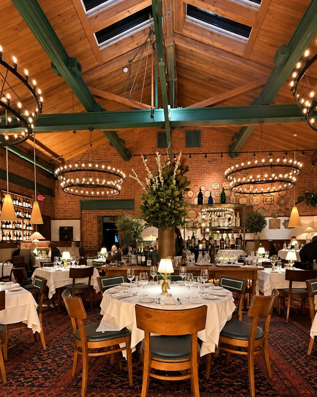 The main dining room at Felice Port Chester, with ring chandeliers, green beams and white tablecloths