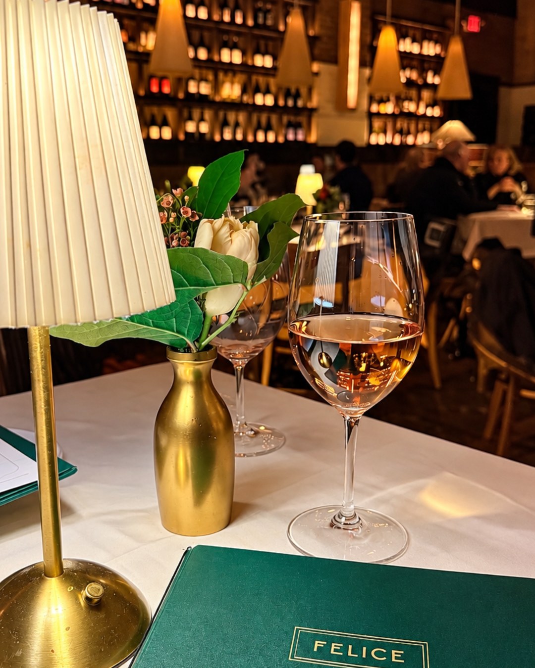 Felice rosé at a lamplit table with the wine wall behind
