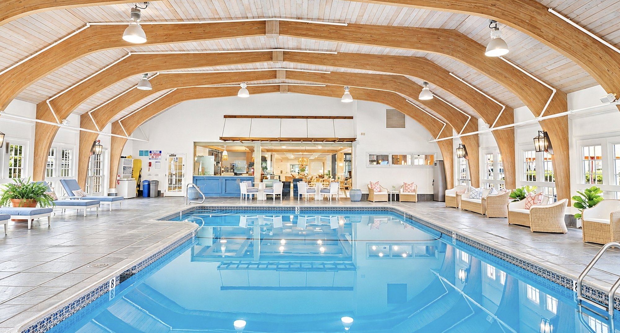 The indoor pool at Nantucket Inn under arched wood beams, with lounge chairs and wicker seating