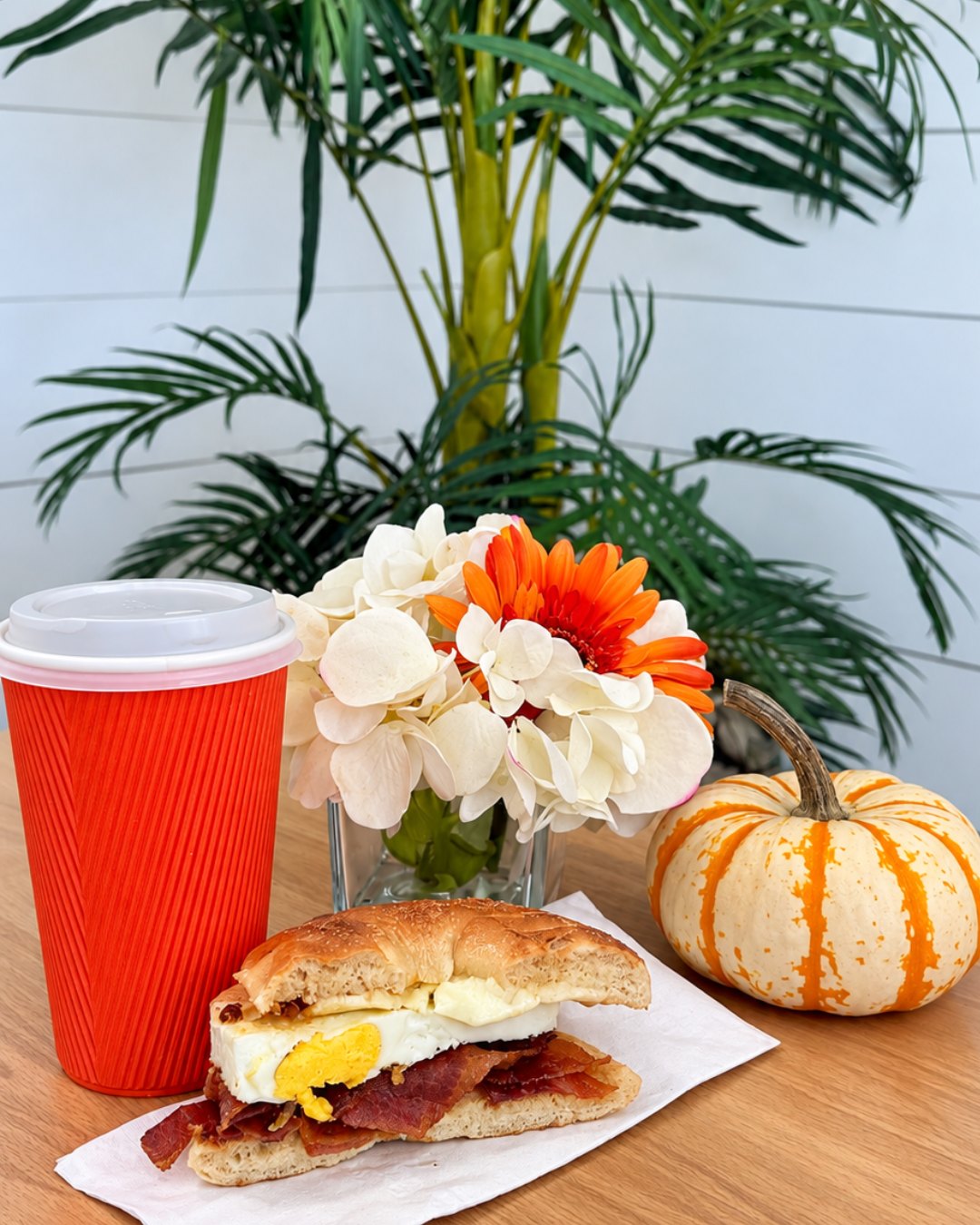 Breakfast sandwich and coffee from Nobadeer Cafe with fresh flowers and a mini pumpkin